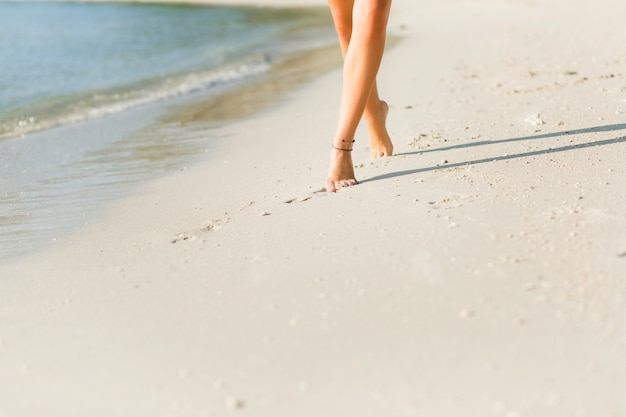 砂の中の日焼けしたスリムな女の子の足のクローズアップ 彼女は水の近くを歩きます 砂は金です 無料の写真