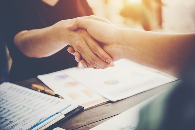 Close-up of two business people shaking hands while sitting at the working place. Free Photo