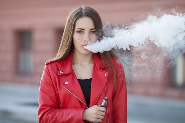 現代の電子タバコの唇を保持しているvaping若い女の子のクローズアップ 禁煙ニコチン 電子タバコのガジェットを持つ若い喫煙者女性 プレミアム写真