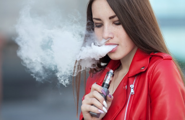 現代の電子タバコの唇を保持しているvaping若い女の子のクローズアップ 禁煙ニコチン 電子タバコのガジェットを持つ若い喫煙者女性 プレミアム写真