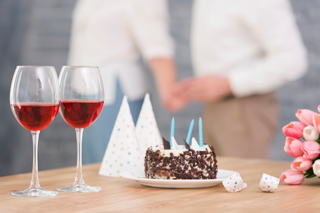 ワイングラスのクローズアップ 美味しいケーキ 木製の机の上のパーティーホーンとチューリップの花 無料の写真