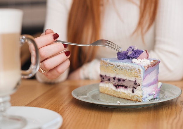木製のテーブルの上皿に美味しいブルーベリーケーキスライス上のフォークを持つ女性のクローズアップ 無料の写真