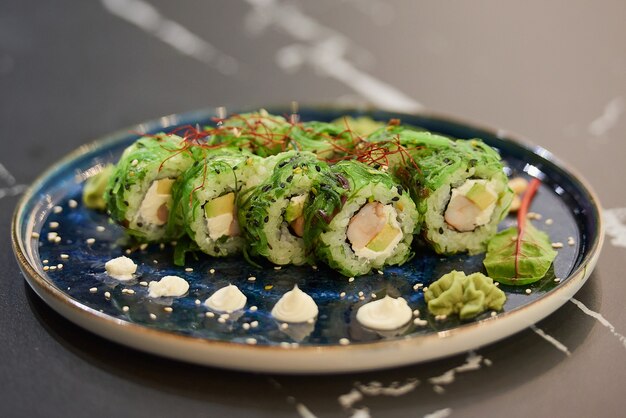 Premium Photo A Close Up Photo Of Sushi Rolls With Chuka Wakame Seaweed Philadelphia Cheese And Shrimps On A Blue Ceramic Plate With Sauce Cashew And Wasabi On A Black Stone Table