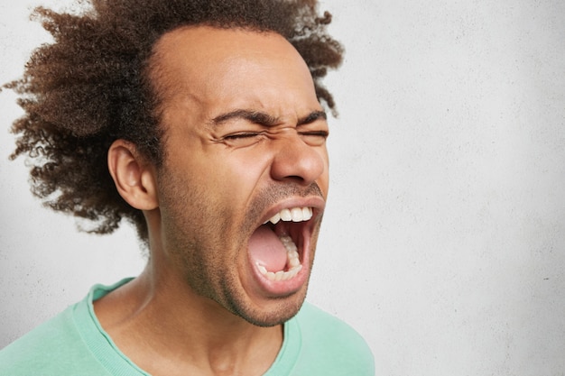 Close up portrait of mad angry young dark skinned male screams in anger and fury Free Photo