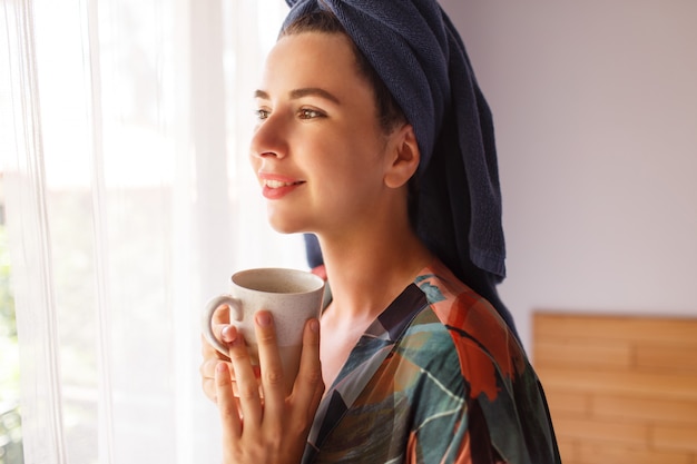 タオルとバスローブに包まれた朝のベッドに座ってお茶を飲んで朝目を覚ますのきれいな女性の肖像画を閉じる 無料の写真
