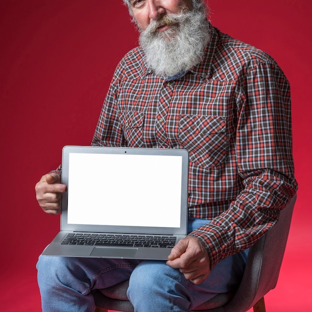 Close-up of senior man showing digital tablet with blank white screen display against red backdrop Free Photo
