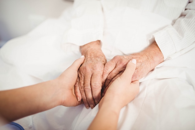 Close-up of senior woman and nurse holding hands Premium Photo