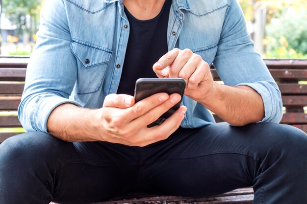 Close up shot of man hands using mobile while sitting on the bench Premium Photo