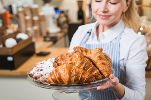 Close-up of a smiling young woman smelling the fresh baked croissants in the cake stand Free Photo