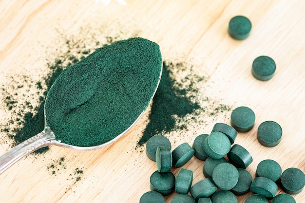 Close up spirulina powder and spirulina pills in spoon , healthy superfood diet and detox nutrition concept Premium Photo