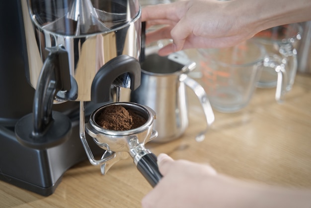 Close up view of barista pulling lever of grinder machine to get grind coffee bean in coffee tamp. Premium Photo