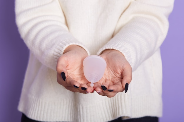 Close up view of faceless woman wearing white shirt holding hydiene product, making choice to use menstrual cup or not, posing isolated on purple,female having period. gynecology concept. Free Photo