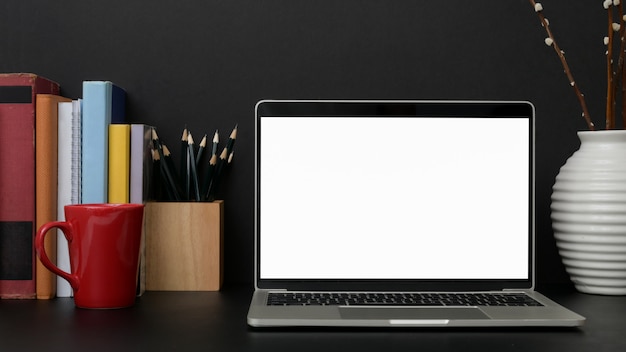 黒いテーブルに空白の画面のノートパソコンで暗い現代の職場のクローズアップ表示 プレミアム写真