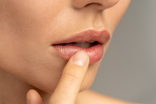 Close up of woman applying moisturizing nourishing balm to her lips with her finger Premium Photo