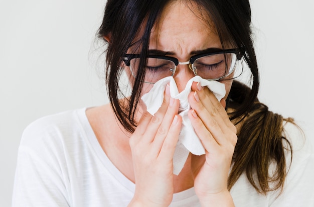 Close-up of a woman blowing her nose in tissue paper against white backdrop Free Photo