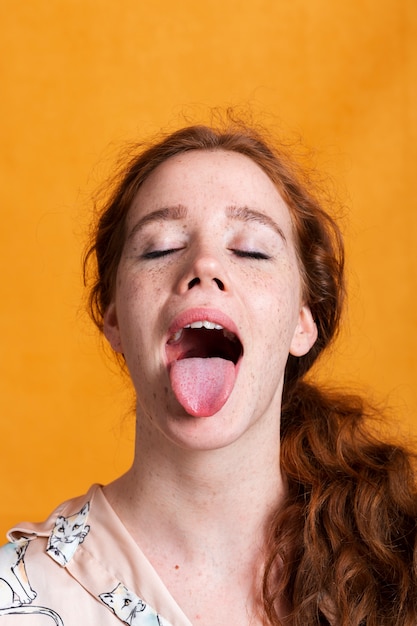 舌出しとオレンジ色の背景を持つクローズアップ女性 プレミアム写真