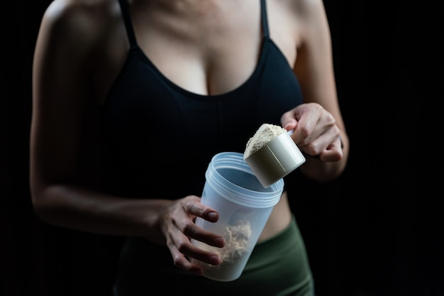 Close up of women with measuring scoop of whey protein and shaker bottle, preparing protein shake. Premium Photo