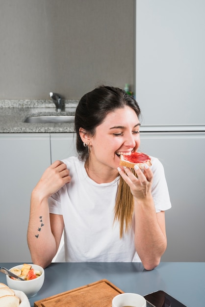 Close-up of a young woman eating jam with bread at breakfast | Free Photo