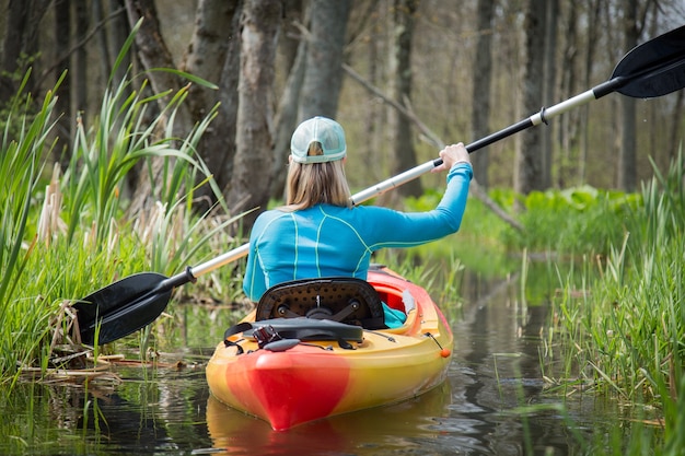 Closeup of a girl kayaking on a small river surrounded by greenery under the sunlight at daytime Free Photo