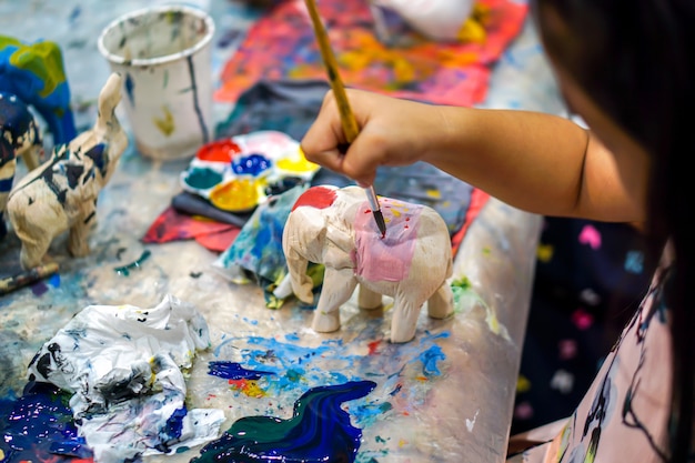 Closeup hands of art students holding paint brush study and learning paint on wood animal doll in the art classroom. Premium Photo