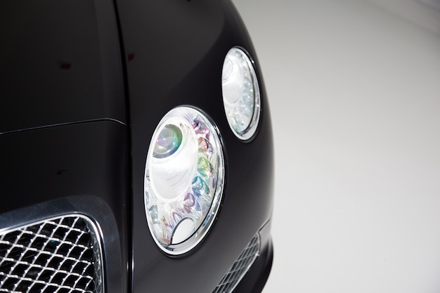 灰色の背景のライトの下で黒い高級車のヘッドライトのクローズアップ 無料の写真