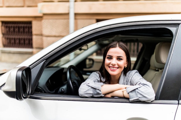 彼女の新しい車に座っている幸せな笑顔の若い魅力的な女性のバイヤーは ディーラーのディーラーロットオフィスの外で隔離された旅行の準備ができて興奮しています 個人輸送自動車購入コンセプト 無料の写真