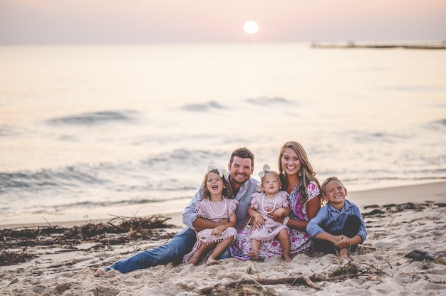 Colpo Del Primo Piano Di Una Famiglia Felice Che Si Siede In Riva Al Mare Al Tramonto Concetto Di Famiglia Foto Gratis