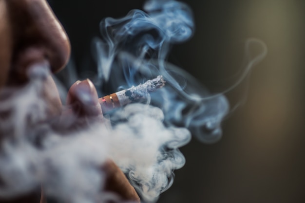 Closeup shot of a person puffing on a cigarette surrounded with smoke Free Photo