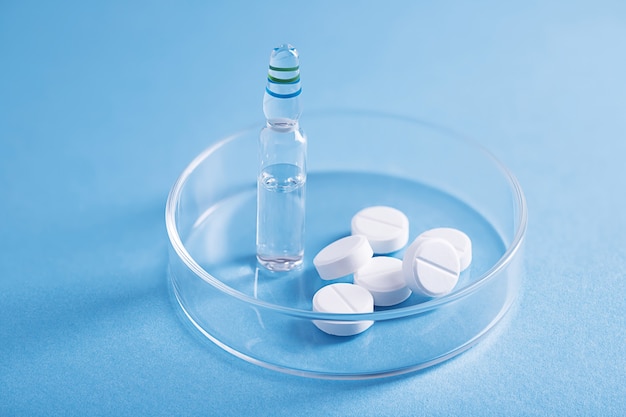 Closeup shot of white pills and a vial of clear liquid in a glass dish at a lab Free Photo