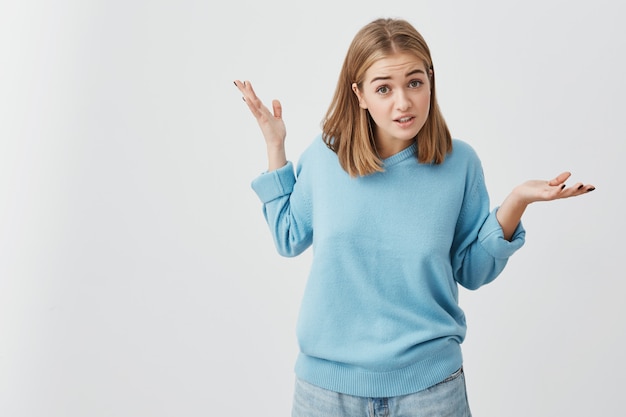 Clueless girl dressed in sweater and jeans shrugging shoulders, staring  with confused look after she did something wrong, not feeling sorry or guilty, not understanding what is wrong. Free Photo