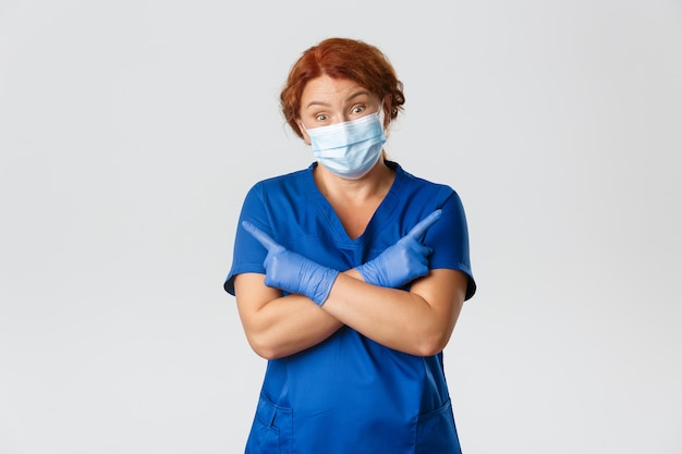 無知な赤毛の女医 フェイスマスクとゴム手袋の看護師は知らない 横向きで肩をすくめる混乱 無料の写真