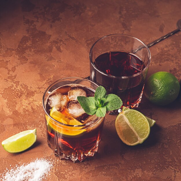 Download Premium Photo Cocktail Of Rum And Cola Ice Cubes And Lime In Glass Goblets On Dark Brown