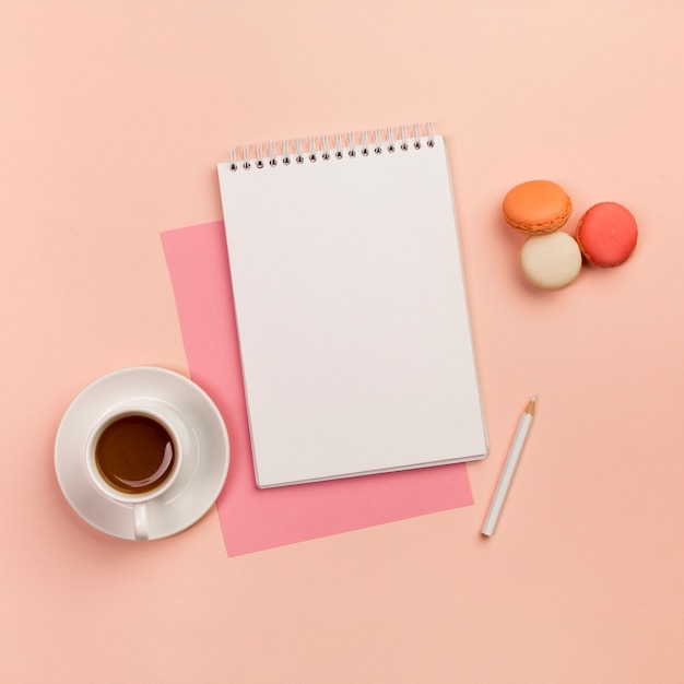 Coffee cup with spiral notepad,white pencil and macaroons on colored backdrop Free Photo