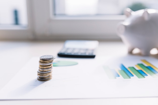 Coin stack on graph with calculator and piggybank over table Free Photo