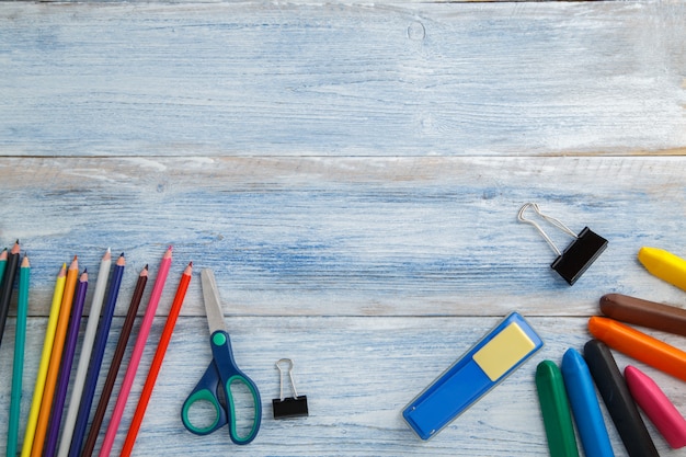 Colored pencils or crayons, scissors, stapler on blue and white scuffed vintage wood, top view Premium Photo