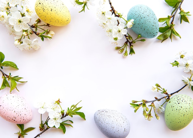 白い背景の上に分離された春の花の花とカラフルなイースターの卵 色付きの卵の休日の境界線 プレミアム写真