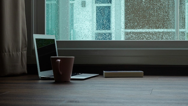 Premium Photo | Computer notebook next to a cup coffee on rainy day window background
