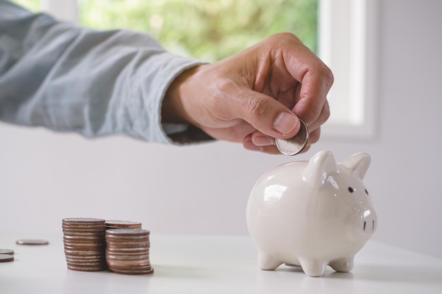Concept saving money for wealth. close up view person putting coin into piggy bank. Premium Photo