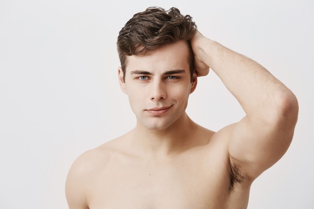 スタイリッシュな散髪と魅力的な目 裸で 黒い髪に触れて ポーズをとる自信のある若いヨーロッパ人 優しく笑顔の健康的なきれいな肌を持つハンサムな男性モデル 無料の写真