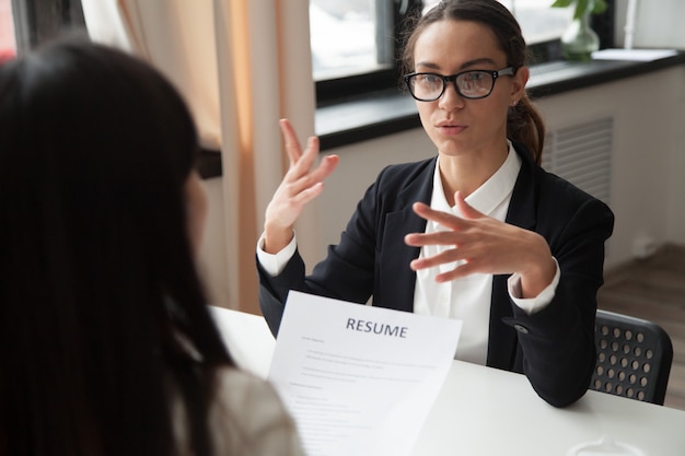 Confident millennial female applicant in glasses talking at job interview Free Photo