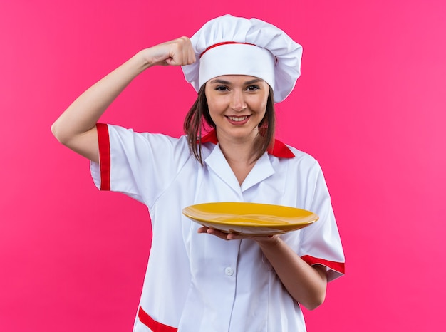 Free Photo Confident Young Female Cook Wearing Chef Uniform Holding Plate Showing Strong 0290