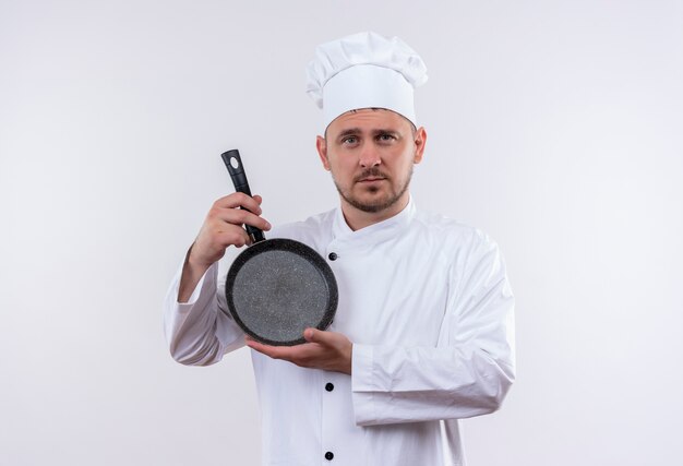 Free Photo Confident Young Handsome Cook In Chef Uniform Holding Frying Pan Isolated On White Wall