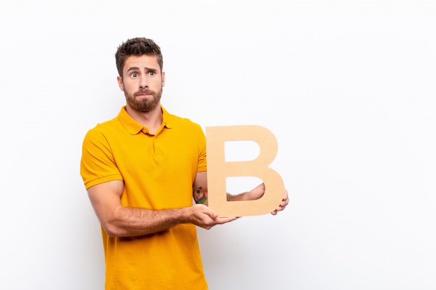 Premium Photo | Confused Young Man Holding The Letter B Of The Alphabet ...