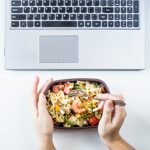 Container with salad with pasta in the workplace near the computer Premium Photo