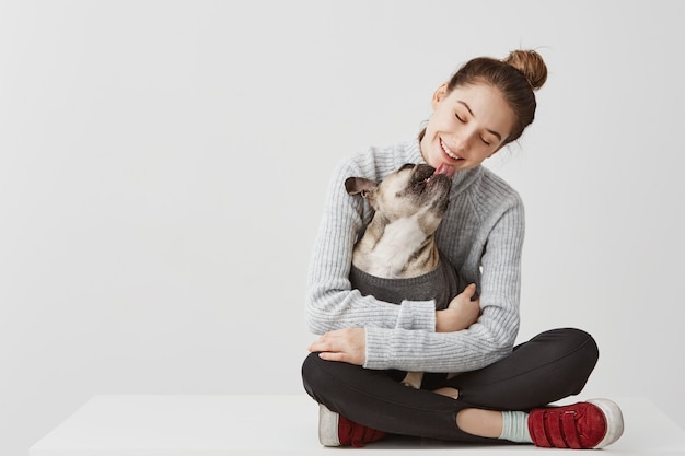 コンテンツ犬を手で保持しているテーブルの上に座っているカジュアルな服装でブルネットの女性 女性のスタートアップデザイナーが血統の犬を抱きしめながら 抱きしめる 喜びの概念 コピースペース 無料の写真