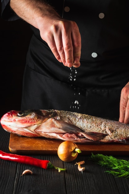 Premium Photo | The cook prepares fresh fish bighead carp sprinkling ...