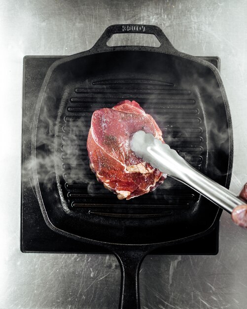 キッチントングでグリル鍋で牛肉ステーキを調理 プレミアム写真