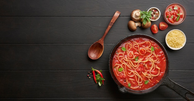Premium Photo Cooking Homemade Italian Pasta Spaghetti With Tomato Sauce In Cast Iron Pan Served With Red Chili Pepper Fresh Basil Cherry Tomatoes And Spices Over Black Rustic Wooden Table