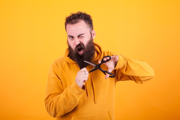 Cool bearded man looking terrified while cutting his beard over yellow background. macho man. lifestyle Free Photo