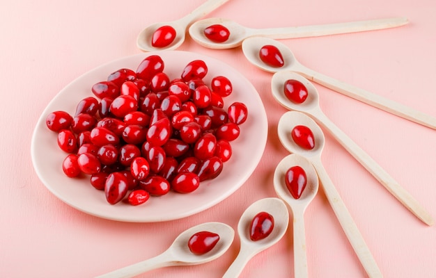 Cornel berries in wooden spoons and plate on pink. high angle view. Free Photo